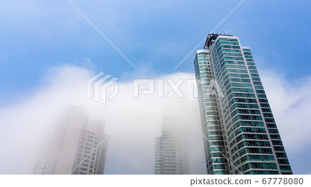 Thick large and heavy mist blow and pass through skyscrapers and cover all other buildings in the area 67778080