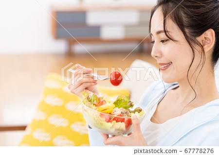 Young woman eating salad on the sofa at home 67778276