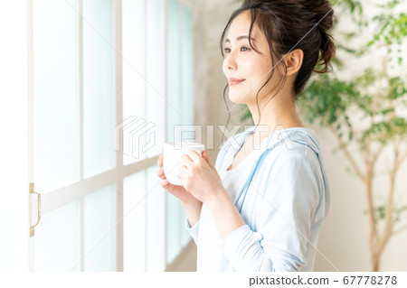 Young woman standing on the windowsill with a cup 67778278