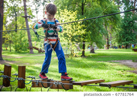 Happy kid playing at adventure park, holding ropes 67781764