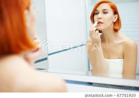 Beautiful girl applies cosmetics on the face in light bathroom. 67781920
