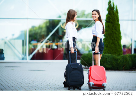 Two happy girls traveling abroad together, carrying suitcase luggage in airport. Two happy girls traveling abroad together, carrying suitcase luggage in airport. 67782562