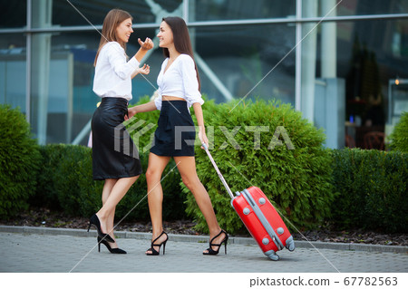 Two happy girls traveling abroad together, carrying suitcase luggage in airport. 67782563
