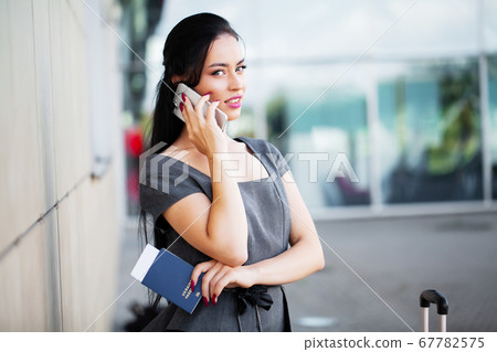 Travel. Business Woman in airport talking on the smartphone while walking with hand luggage in airport going to gate Travel. Business Woman in airport talking on the smartphone while walking with hand luggage in airport going to gate 67782575