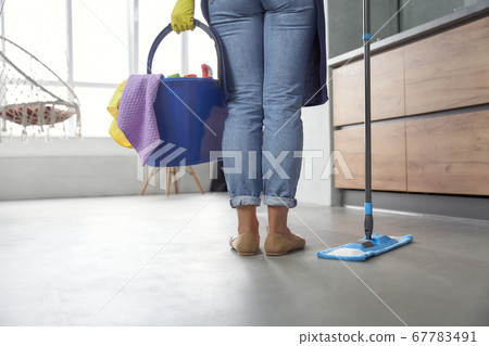 Washing floor. Back view of woman holding mop and plastic bucket or basket with rags, detergents and different cleaning products while standing in the modern kitchen Washing floor. Back view of woman holding mop and plastic bucket or basket with rags, detergents and different cleaning products while standing in the modern kitchen 67783491