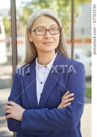 Portrait of confidence and success. Beautiful mature business woman wearing eyeglasses, looking aside and thinking about something while standing outdoors 67783510