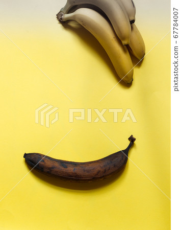 one spoiled banana and a bunch of fresh bananas on a yellow background, top view 67784007
