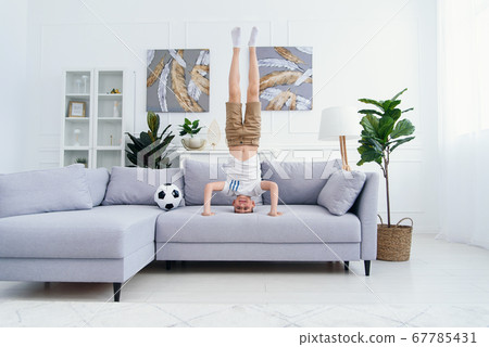 12-s aged sporty acrobat boy standing on his head and hands on couch at home. 12-s aged sporty acrobat boy standing on his head and hands on couch at home. 67785431