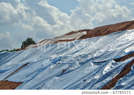 SEREMBAN, MALASIA - MARCH 3, 2019: The plastic sheet is spread over the surface of the slope to prevent erosion. Also to temporarily stabilize the slope before the permanent stabilization work done. SEREMBAN, MALASIA - MARCH 3, 2019: The plastic sheet is spread over the surface of the slope to prevent erosion. Also to temporarily stabilize the slope before the permanent stabilization work done. 67785571