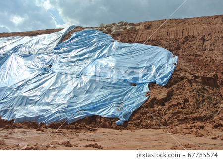 SEREMBAN, MALASIA - MARCH 3, 2019: The plastic sheet is spread over the surface of the slope to prevent erosion. Also to temporarily stabilize the slope before the permanent stabilization work done. SEREMBAN, MALASIA - MARCH 3, 2019: The plastic sheet is spread over the surface of the slope to prevent erosion. Also to temporarily stabilize the slope before the permanent stabilization work done. 67785574