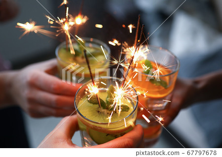 Three hands hold three glasses with cocktail and sparklers close-up. Three hands hold three glasses with cocktail and sparklers close-up. 67797678