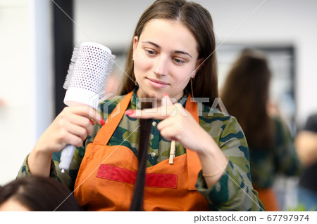 Beautiful woman in apron hold long strand of hair close-up and comb. 67797974