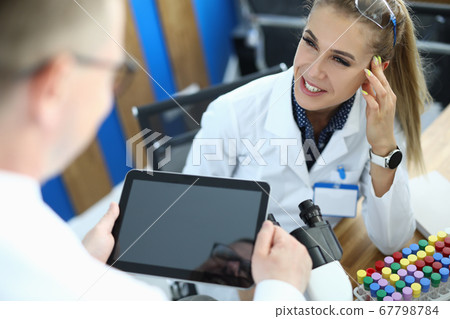 Female laborant sit on chait, examines biomaterial with microscope and communicate with pacient in clinic. Female laborant sit on chait, examines biomaterial with microscope and communicate with pacient in clinic. 67798784