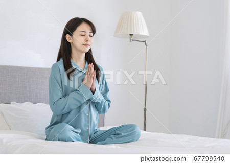 Morning yoga Young woman meditating in pajamas on bed Morning yoga Young woman meditating in pajamas on bed 67799540