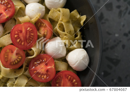 fettuccine pasta with pesto, mozzarella and cherry tomatoes in black bowl on concrete background 67804087