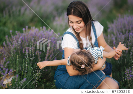 Portrait of young mom with her adorable daughter in summer lavender field. Family denim style. Woman in straw hat. Mom tickle daughter Portrait of young mom with her adorable daughter in summer lavender field. Family denim style. Woman in straw hat. Mom tickle daughter 67805258
