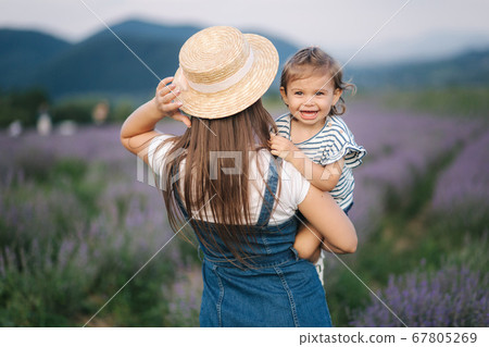 Portrait of young mom with her adorable daughter in summer lavender field. Family denim style. Woman in straw hat Portrait of young mom with her adorable daughter in summer lavender field. Family denim style. Woman in straw hat 67805269