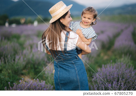 Portrait of young mom with her adorable daughter in summer lavender field. Family denim style. Woman in straw hat Portrait of young mom with her adorable daughter in summer lavender field. Family denim style. Woman in straw hat 67805270