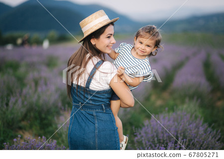Portrait of young mom with her adorable daughter in summer lavender field. Family denim style. Woman in straw hat Portrait of young mom with her adorable daughter in summer lavender field. Family denim style. Woman in straw hat 67805271