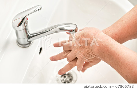Senior woman washing her hands with soap under tap Senior woman washing her hands with soap under tap 67806788