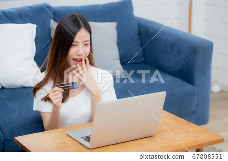 Young asian woman sit on sofa using laptop computer shopping online with credit card buy to internet 67808551