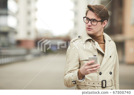 Young Businessman Holding Smartphone Outdoors in City Young Businessman Holding Smartphone Outdoors in City 67808740