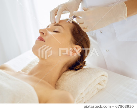 Beautiful woman receiving beauty injections with closed eyes. Beautician doctor hands doing beauty procedure to female face with syringe. Cosmetic medicine and surgery concept Beautiful woman receiving beauty injections with closed eyes. Beautician doctor hands doing beauty procedure to female face with syringe. Cosmetic medicine and surgery concept 67808930