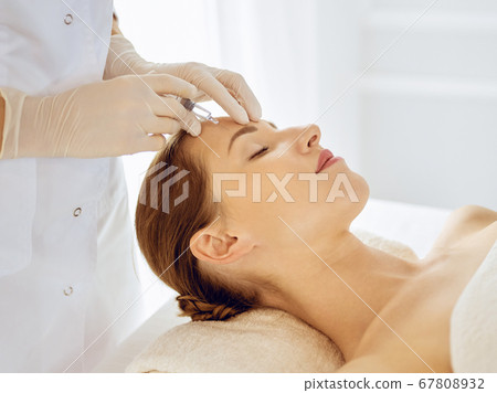 Beautiful woman receiving beauty injections with closed eyes. Beautician doctor hands doing beauty procedure to female face with syringe. Cosmetic medicine and surgery concept 67808932