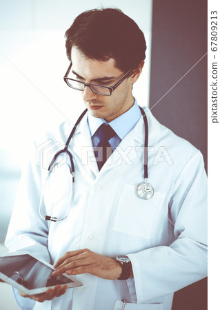 Doctor man using tablet computer for network research or virtual disease treatment. Perfect medical service in clinic. Modern medicine, medic data and healthcare concepts Doctor man using tablet computer for network research or virtual disease treatment. Perfect medical service in clinic. Modern medicine, medic data and healthcare concepts 67809213