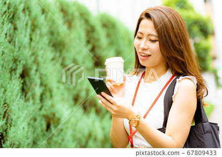 [Business scene] A young office lady with a smiling face who uses a smartphone while working in a coffee shop [Summer] 67809433