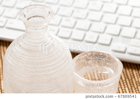 Online drinking party image. A glass sake bottle containing sake and a computer keyboard. Online drinking party image. A glass sake bottle containing sake and a computer keyboard. 67809541