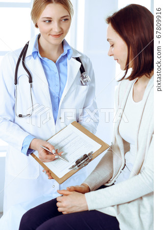 Young woman doctor and patient at medical examination at hospital office. Blue color blouse of therapist looks good. Medicine and healthcare concept Young woman doctor and patient at medical examination at hospital office. Blue color blouse of therapist looks good. Medicine and healthcare concept 67809916