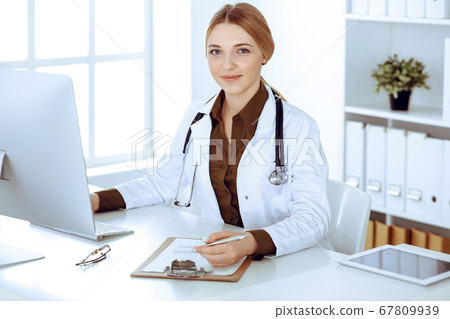 Young woman doctor at work in hospital looking at desktop pc monitor. Physician controls medication history records and exam results. Medicine and healthcare concept Young woman doctor at work in hospital looking at desktop pc monitor. Physician controls medication history records and exam results. Medicine and healthcare concept 67809939