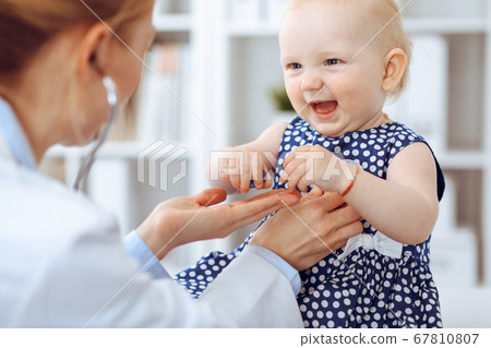Doctor and patient in hospital. Little girl dressed in dark blue dress in peas is being examined by doctor with stethoscope. Medicine concept Doctor and patient in hospital. Little girl dressed in dark blue dress in peas is being examined by doctor with stethoscope. Medicine concept 67810807