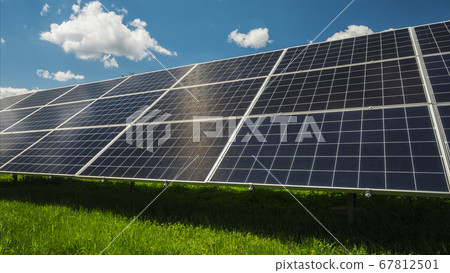 Solar panels against the blue sky with clouds and green grass below Solar panels against the blue sky with clouds and green grass below 67812501