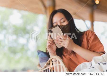 Woman in face mask using her mobile phone while sitting in a chair. Woman in face mask using her mobile phone while sitting in a chair. 67813166