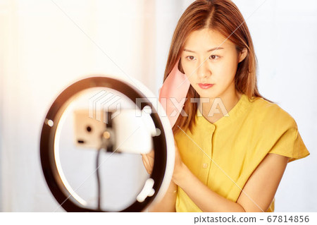 Young woman putting on mask in front of smartphone camera Young woman putting on mask in front of smartphone camera 67814856