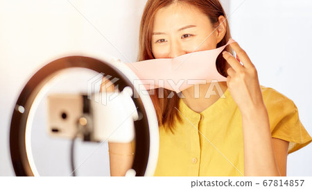Young woman putting on mask in front of smartphone camera 67814857