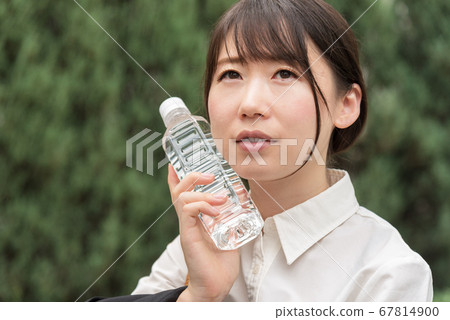An outside business woman who cools down with a plastic bottle 67814900