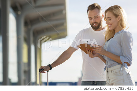 Travel concept. Lovely couple checking tickets outside Travel concept. Lovely couple checking tickets outside 67823435