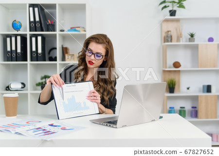 Confident experienced successful business woman in stylish clothes and glasses talking with her business partner by video call and shows report with graphs. Confident experienced successful business woman in stylish clothes and glasses talking with her business partner by video call and shows report with graphs. 67827652