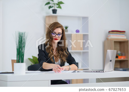 Attractive young office woman in formal wear works with business paperwork at the desk. Attractive young office woman in formal wear works with business paperwork at the desk. 67827653