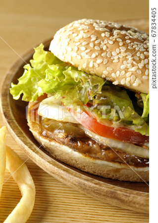 Teriyaki burger and spilling potato fries on a round wooden plate 67834405