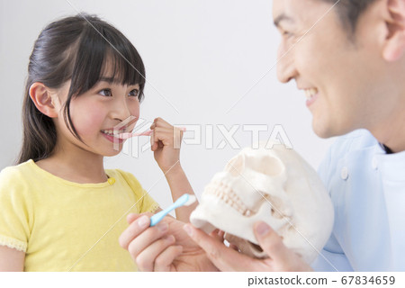 Male dentist teaching girls brushing teeth 67834659