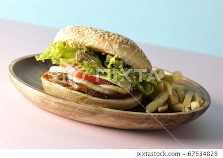 Teriyaki burger and potato fries on a wooden plate taken using two background papers of pink and light blue 67834828