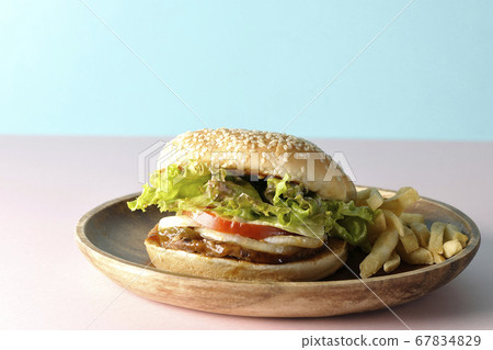 Teriyaki burger and potato fries on a wooden plate taken using two background papers of pink and light blue 67834829