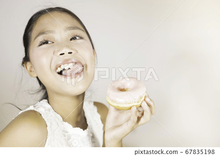 A cute Asian girl is enjoying eating donuts. 67835198