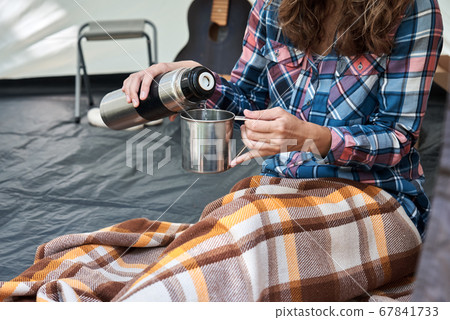 Woman pouring tea from thermos in the camping tent Woman pouring tea from thermos in the camping tent 67841733