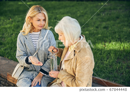 Mature lady feeling ill near female friend in the park Mature lady feeling ill near female friend in the park 67844448