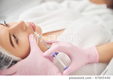 Calm young woman getting cosmetic facial treatment 67845440